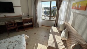 A hotel room with a bed, a sofa, a desk with a chair, a TV, and a window with curtains.