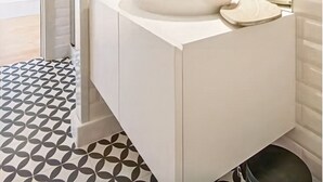 Un baño moderno con un lavamanos blanco, un espejo grande y un piso estampado.