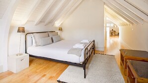 Un dormitorio con cama, lámparas de noche, piso de madera y vista al pasillo.
