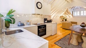 Una cocina moderna con encimera de mármol, horno empotrado y cafetera. Hay una zona de comedor con una mesa y sillas de madera, y un sofá.