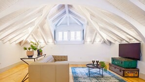 Un loft espacioso con techo alto, un ventanal grande, un sofá, una mesa de centro y un televisor.
