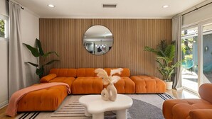 A modern living room with a large orange sectional sofa, a white coffee table, and a large mirror on the wall. - Trendy Getaway | Hot Tub | 20 mins to Disney (Long Beach)