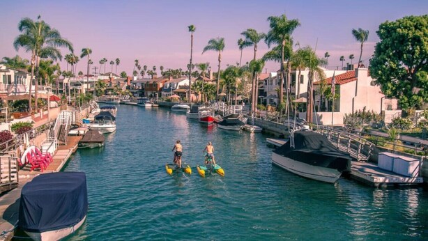A marina with boats docked, palm trees lining the water, and a couple riding jet skis. - Trendy Getaway | Hot Tub | 20 mins to Disney (Long Beach)