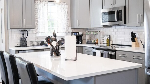 A modern kitchen with grey cabinets, a white island, and stainless steel appliances.