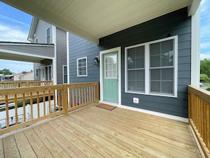 Um deck de madeira com uma porta verde e janelas emolduradas por branco.