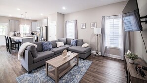 A modern living room with a grey sectional sofa, a wooden coffee table, and a blue patterned rug.