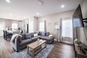 Uma sala de estar moderna com um sofá modular cinzento, uma mesa de centro de madeira e um tapete azul estampado.
