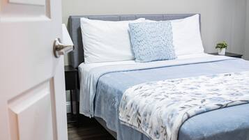 A neatly made bed with a blue and white floral bedspread, a white pillow, and a blue knitted throw.