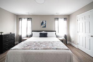 Um quarto com uma cama, mesas de cabeceira, cômoda e uma porta.