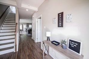 Interior moderno com escada, placa de boas-vindas e escrivaninha com luminária e mensagem emoldurada.