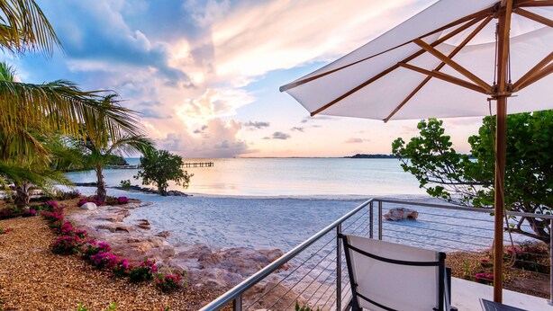 Eine Terrasse am Strand mit Blick auf das Meer, einem Holz Sonnenschirm und einem Stuhl.