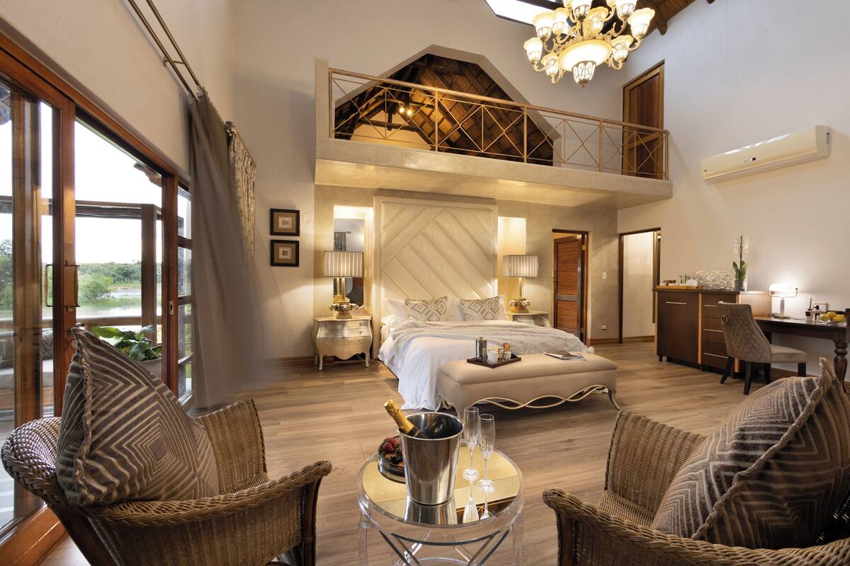 Une chambre spacieuse avec un grand lit, un balcon et un coin repas aménagé avec des meubles en osier.