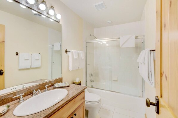 A modern bathroom with a large mirror, a sink, a shower, and a toilet. - Ranch Creek Log Home (Fraser)