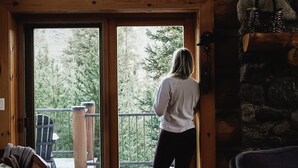 A woman standing at a wooden door with a view of a snowy deck and trees. - Ranch Creek Log Home (Fraser)