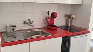 Een kleine keuken met een rode aanrecht, een roestvrijstalen spoelbak en witte kastjes.