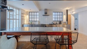Une cuisine moderne dotée d’un grand îlot central, de deux chaises au design épuré en métal noir et d’une table en bois.