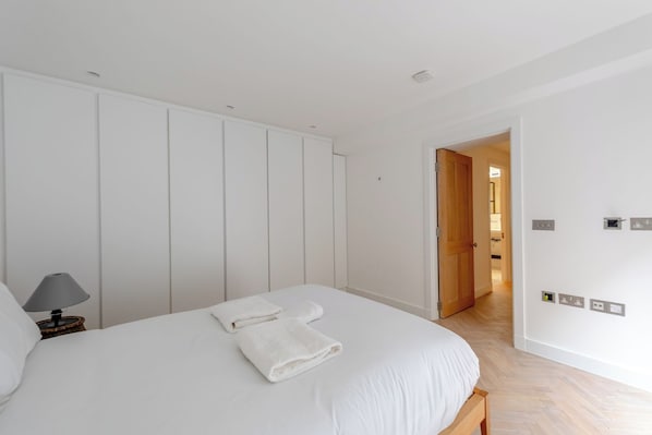 A bedroom with a bed, a nightstand, a wooden door, and a hallway leading to a bathroom.