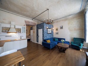 A spacious living area with a kitchen, a blue sofa, a wooden coffee table, and a teal armchair.
