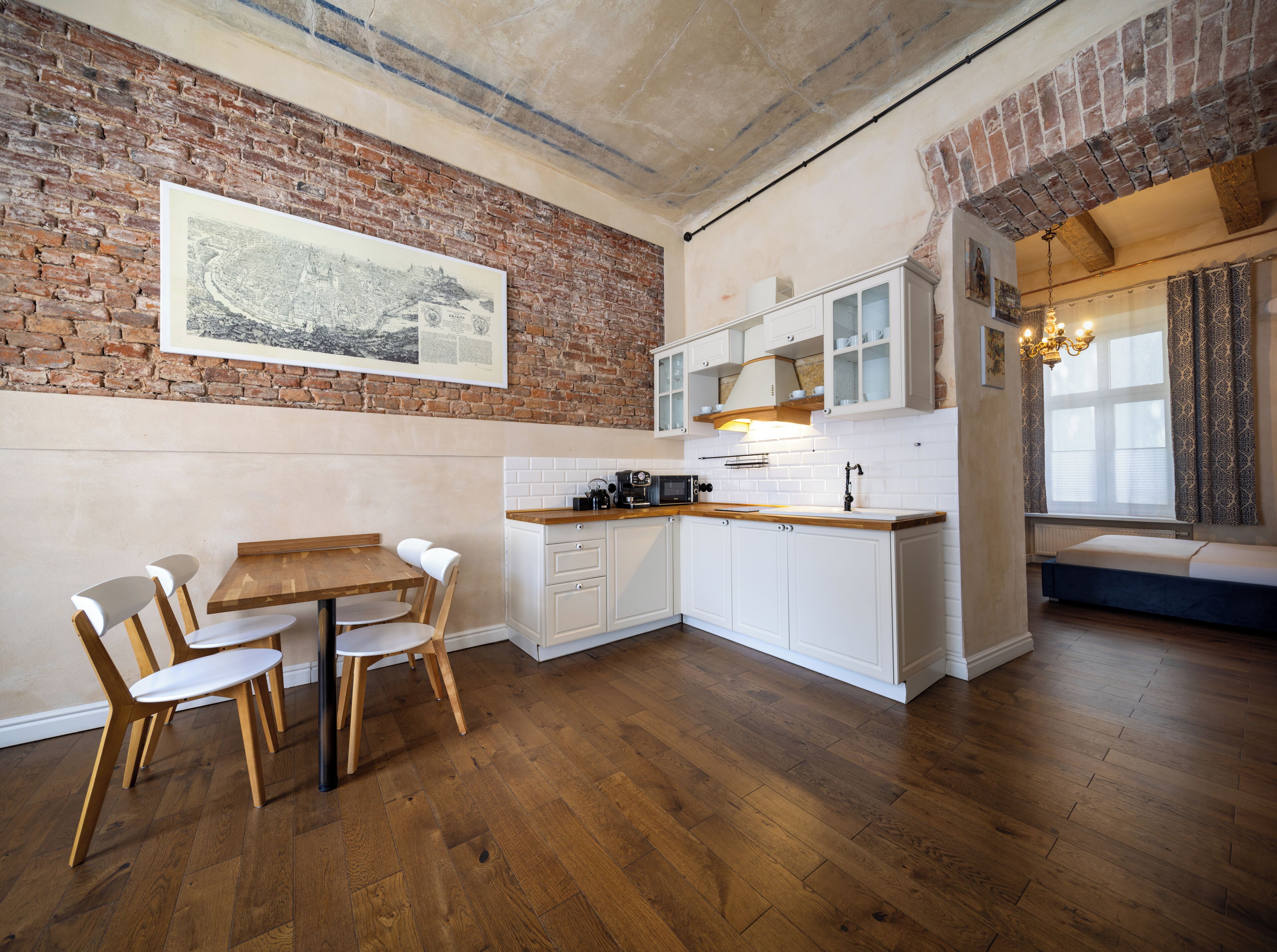 A kitchen with a brick wall, wooden floor, white cabinets, and a dining area with chairs.