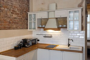 A kitchen with white cabinetry, a brick wall, and a wooden countertop.