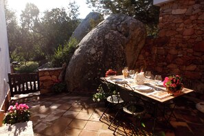 Un espace de restauration en plein air, agrémenté d’un mur en pierre, d’un grand rocher et d’une table dressée pour deux personnes, avec des chaises.