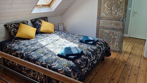 A bedroom with a sloped ceiling, a skylight, a bed with floral bedding, and a rustic door.