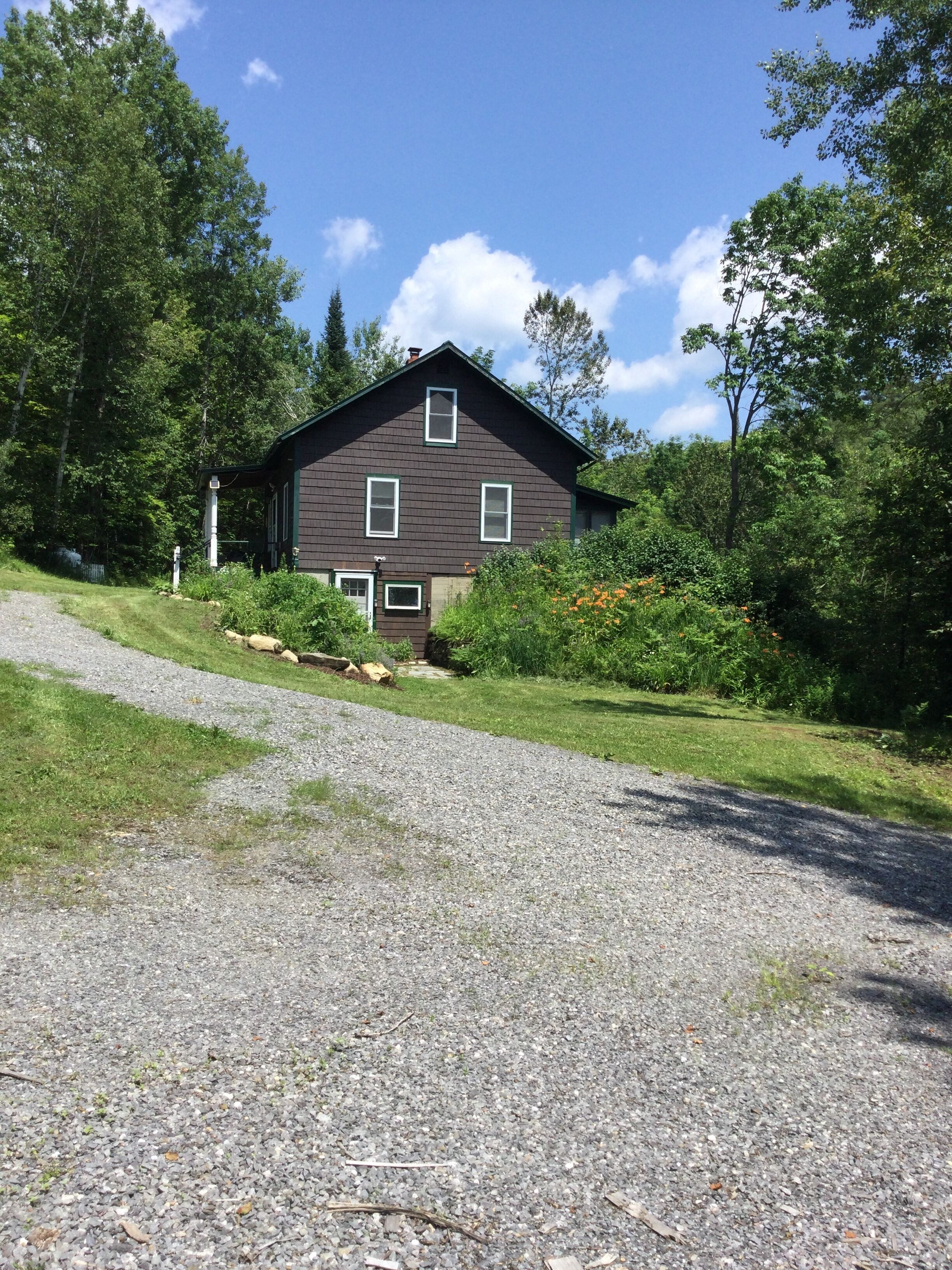 A two-story house with a gravel driveway and a grassy area in front.