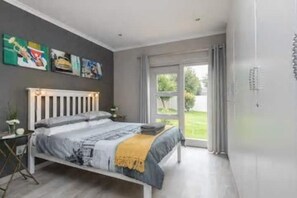Ein Schlafzimmer mit Bett, Nachttisch, Fenster und Tür.