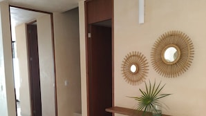 A hallway with a wooden door, a wall-mounted shelf with a plant, and two wall-mounted mirrors. - Surenna Bella - 3 Bedroom Home With Pool (Tulum)