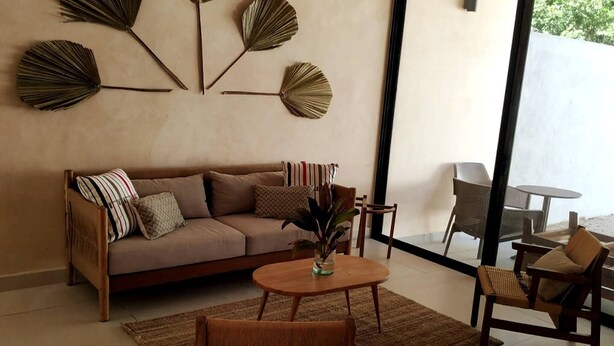 A living room with a sofa, a coffee table, and a chair. There are wall decorations and a view through a glass door. - Surenna Bella - 3 Bedroom Home With Pool (Tulum)
