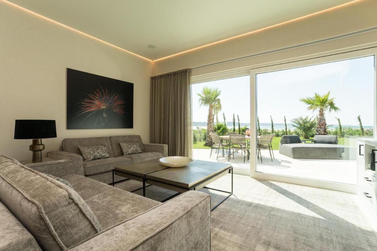 Un salon moderne avec un canapé, une table basse et des œuvres d’art, donnant sur un balcon aménagé avec du mobilier d’extérieur et offrant une vue sur la mer.