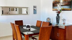 Un coin repas avec une table à plateau en verre, des chaises en bois, un ventilateur de plafond et un tableau accroché au mur.