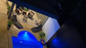 Une piscine éclairée de lumière bleue, entourée de chaises longues et de plantes en pot.
