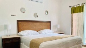 Une chambre d’hôtel avec un grand lit, deux tables de chevet avec des lampes, une tête de lit en bois et une fenêtre avec des rideaux.