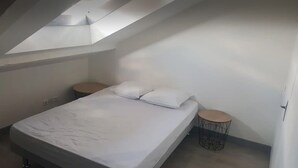 Un dormitorio con cama, dos mesitas de noche y un tragaluz.
