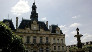 Un edificio histórico con una torre de reloj, una fuente y un jardín bien cuidado.