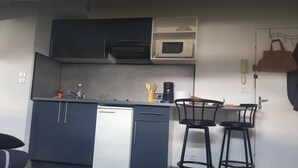 Una cocina compacta con armarios oscuros, microondas, cafetera y un pequeño comedor con dos taburetes.
