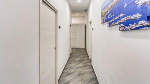 Un pasillo estrecho con piso de madera, paredes blancas y un gran mural azul que representa una escena de puerto.