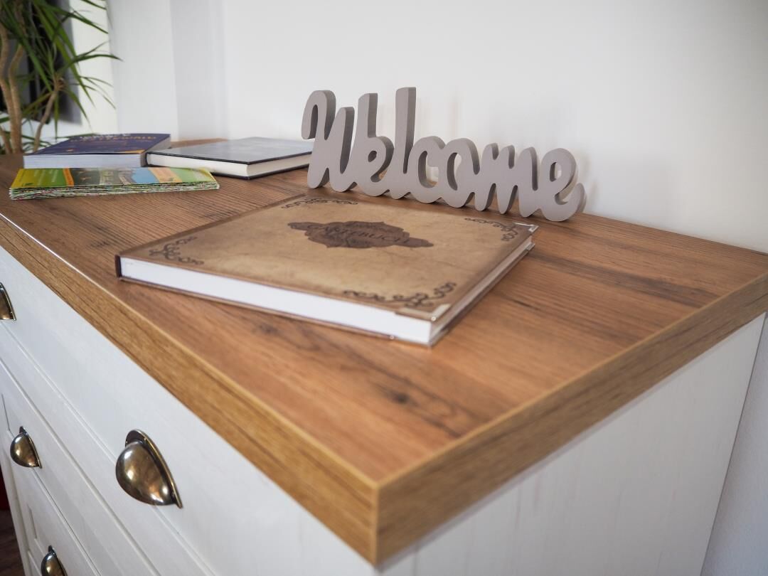 Een houten bureau met een bordje welkomstwoord, een boek en een plant.