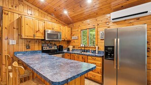 Une cuisine rustique, située dans une cabane en bois, avec un comptoir en granit, des appareils électroménagers en acier inoxydable et un grand réfrigérateur.