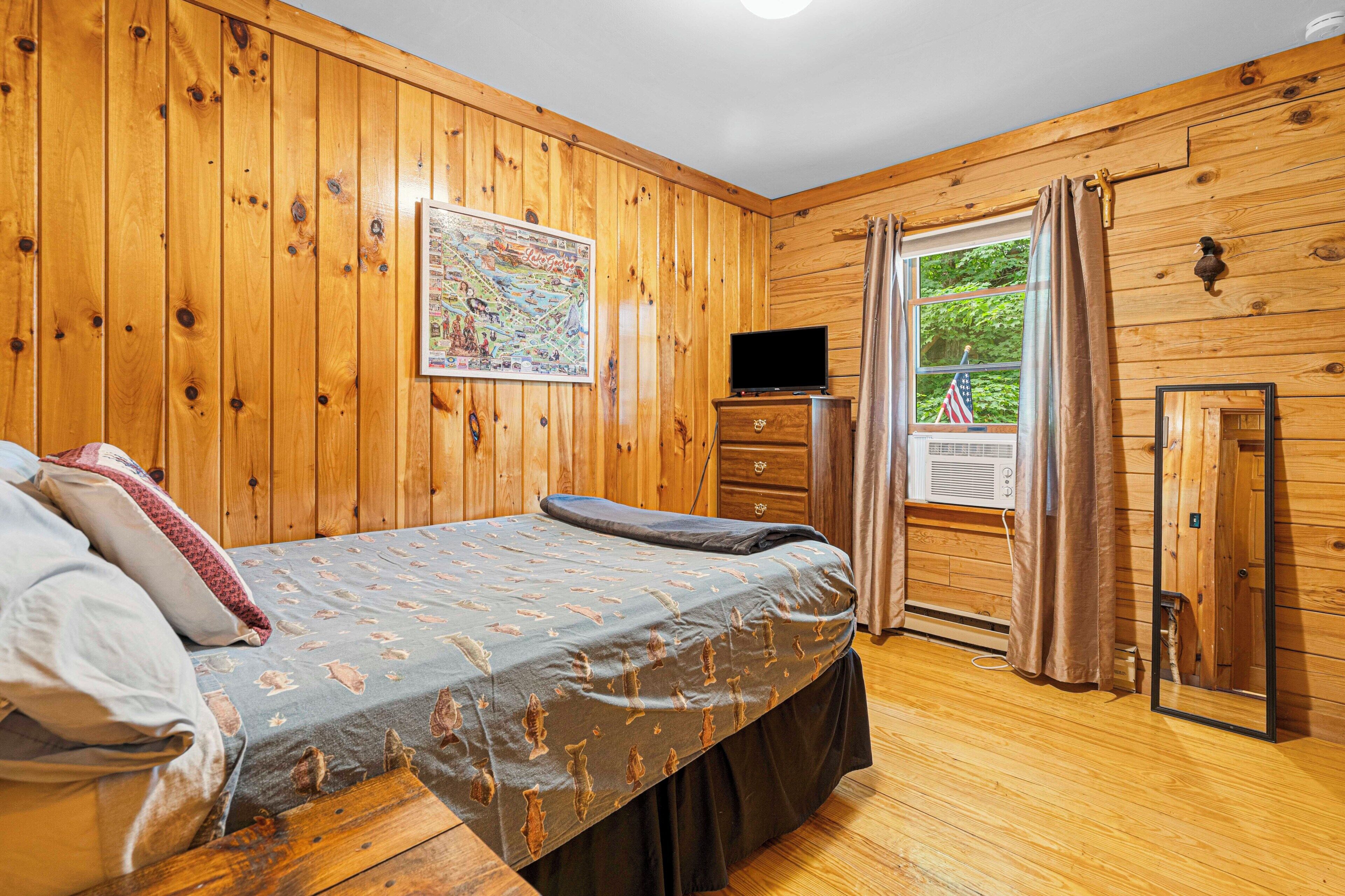 A wooden-paneled room with a bed, a television, and a window with curtains.
