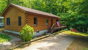 Une cabane en rondins avec une véranda, un drapeau et des sièges d’extérieur.