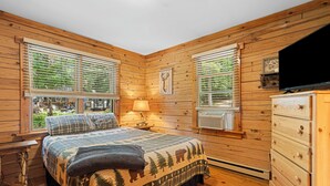 Une chambre dans une cabane en bois, avec un lit, une commode et deux fenêtres équipées de stores.