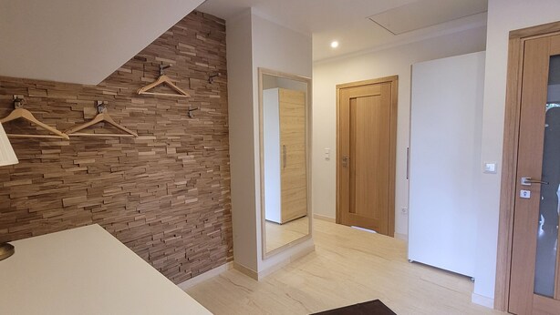 A modern hotel room with a wooden wall, a white desk, a lamp, a mirror, and a door.