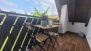 A balcony with a wooden table, two chairs, a potted plant, and a candle.