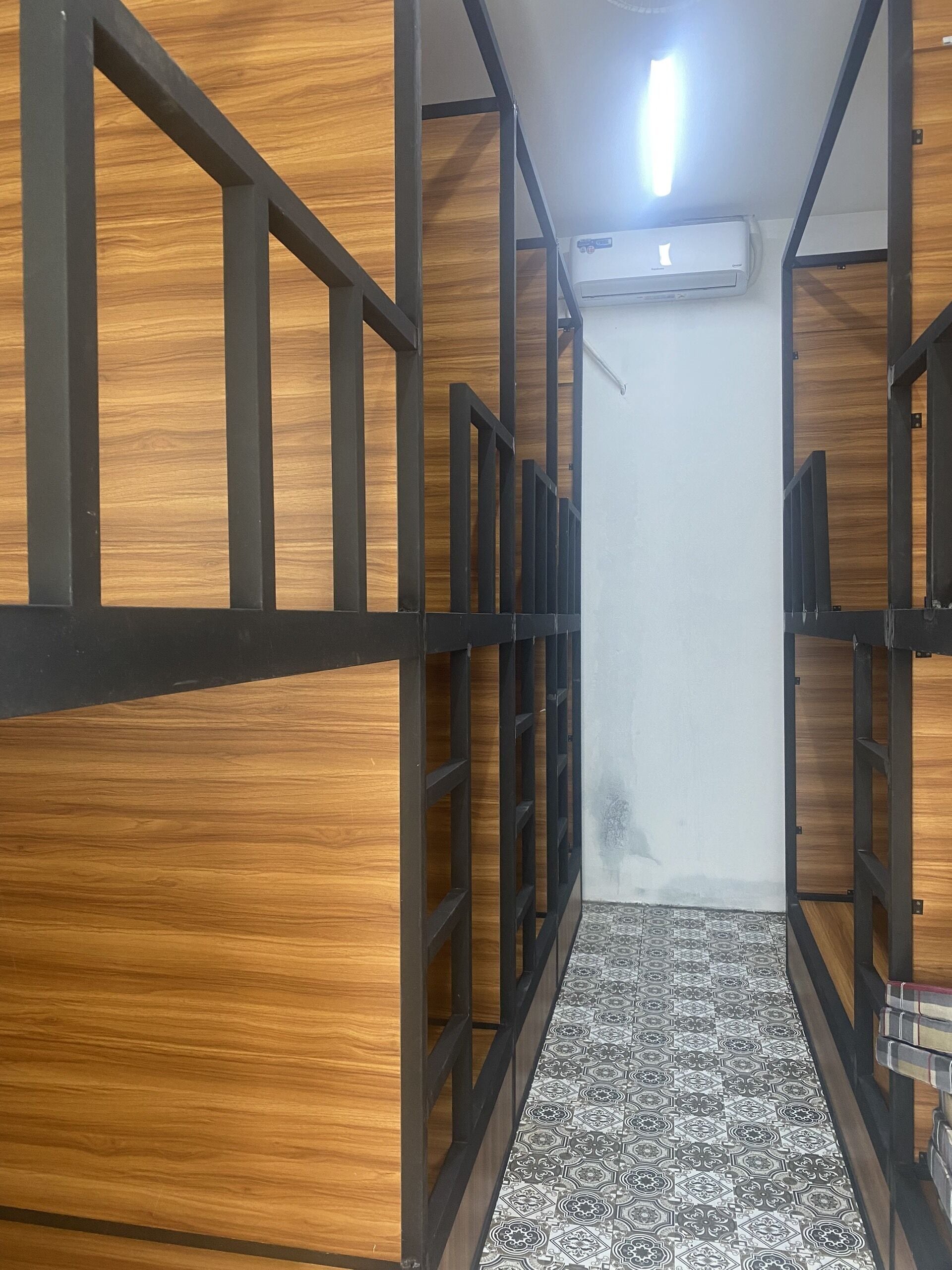 Un pasillo estrecho con paneles de madera y barandillas de metal negro, que conduce a una habitación con suelo estampado.