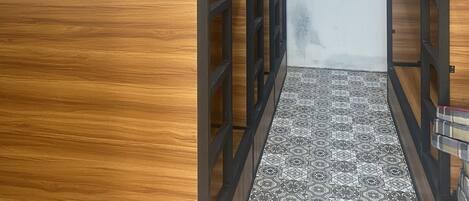 Un pasillo estrecho con paneles de madera y barandillas de metal negro, que conduce a una habitación con suelo estampado.