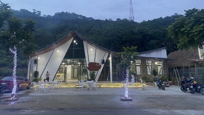 A modern building with a triangular roof and large windows, surrounded by outdoor seating and decorative lights. - Quiri Peninsula Hostel (Ha Giang 1)