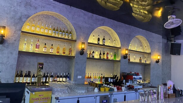 A bar area with multiple shelves of liquor bottles, a bar counter with glasses and a coffee machine, and a sign for NPP TUAN CHIVAS. - Quiri Peninsula Hostel (Ha Giang 1)