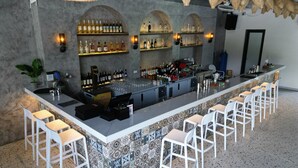 A bar area with a long counter, multiple shelves of bottles, and white bar stools. - Quiri Peninsula Hostel (Ha Giang 1)